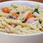 white bowl with bacon, tomatoes, spinach, white sauce, and penne noodles
