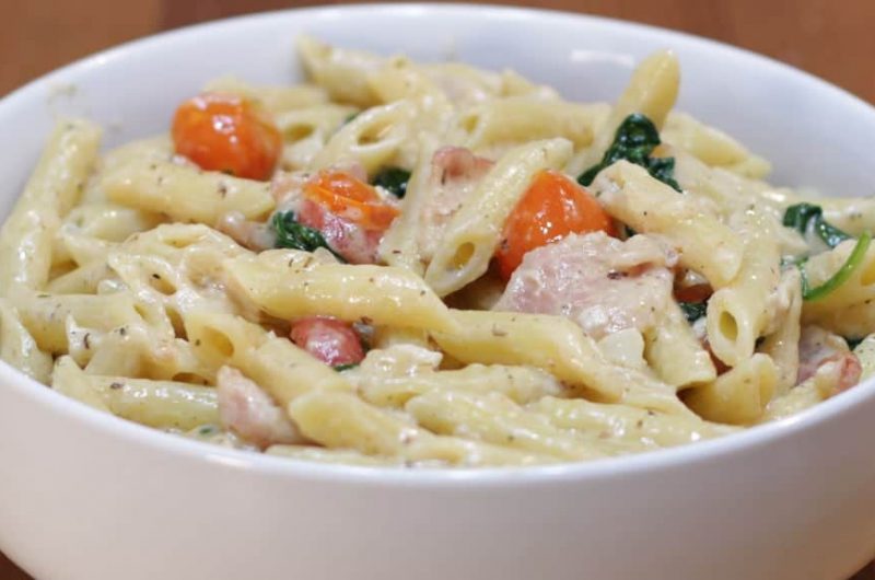 white bowl with bacon, tomatoes, spinach, white sauce, and penne noodles