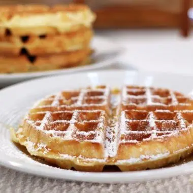 restaurant style belgian waffles on a white plate with powdered sugar