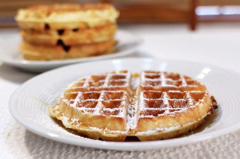 restaurant style belgian waffles on a white plate with powdered sugar