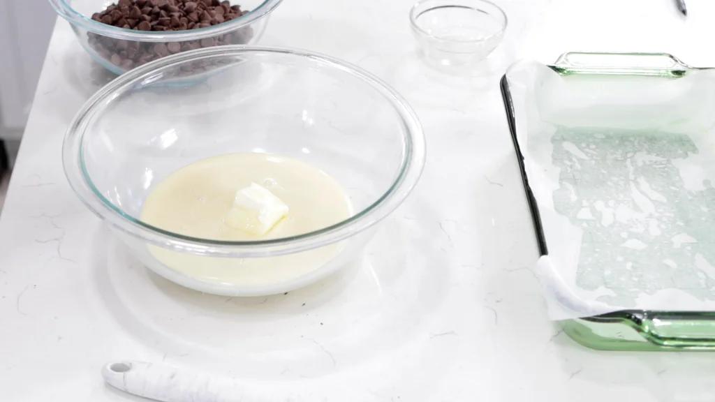 Butter and sweetened condensed milk in a medium bowl on a white counter. Butter and sweetened condensed milk in a medium bowl on a white counter.