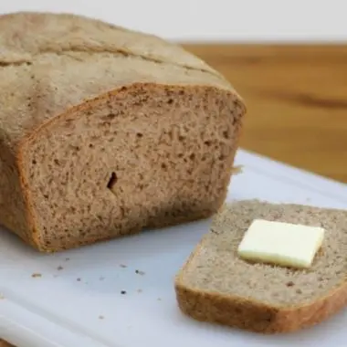 Acorn bread on white cutting board slice has butter on it