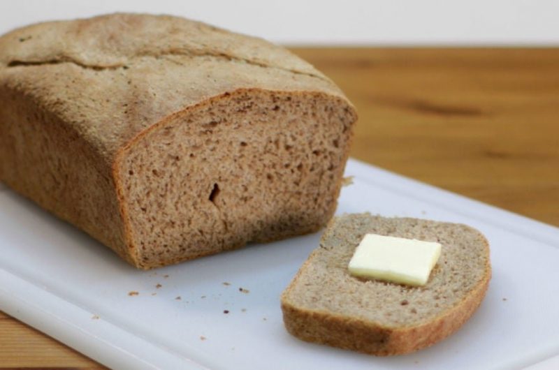 Acorn bread on white cutting board slice has butter on it