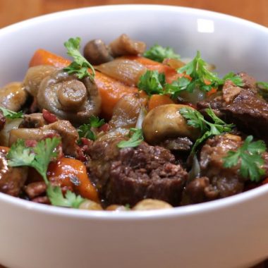 A large white bowl of beef bourguignon on a wooden table