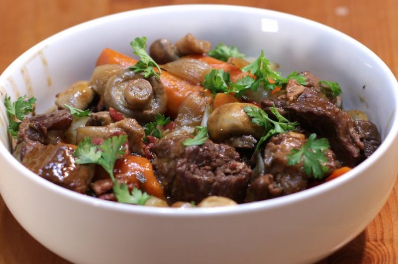 A large white bowl of beef bourguignon on a wooden table