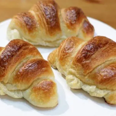 Three homemade croissants sitting on white cake pedestal.