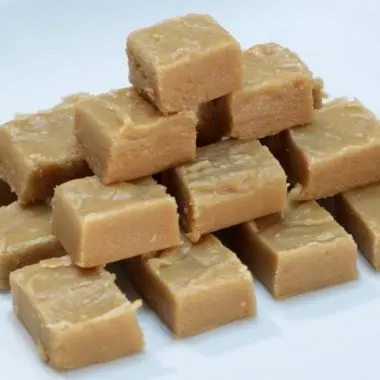 Peanut butter fudge cut in cubes stacked on a white plate