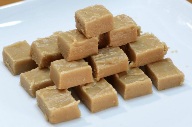 Peanut butter fudge cut in cubes stacked on a white plate