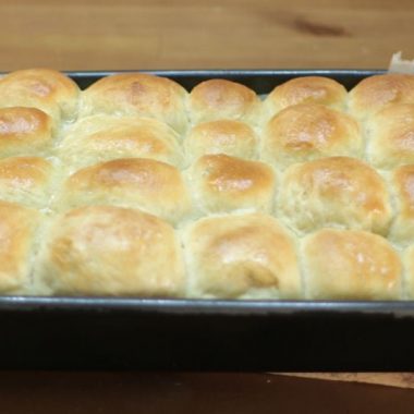 soft no knead dinner rolls in a dark gray pan on a wooden table