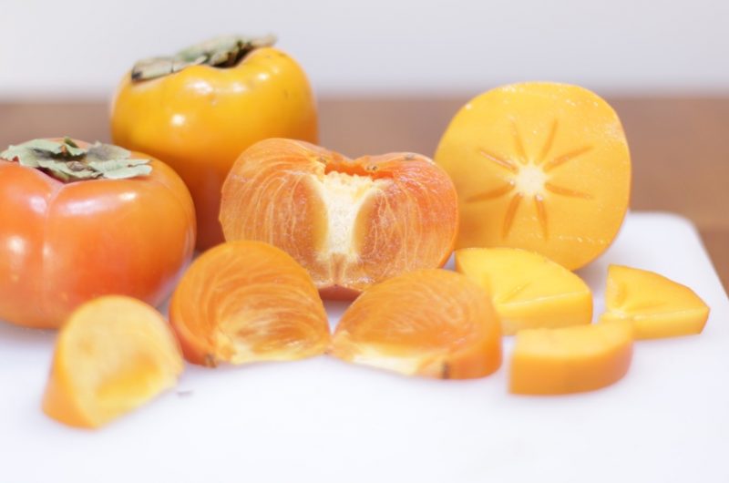 how to eat a persimmon three persimmons cut up on a white cutting board on a wooden table