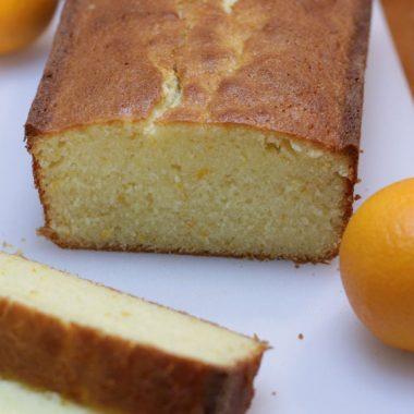 Orange cake on a white cutting board with oranges