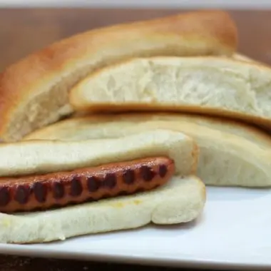 Homemade hot dog buns on a white plate on a wooden table