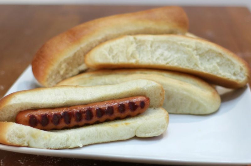 Homemade hot dog buns on a white plate on a wooden table