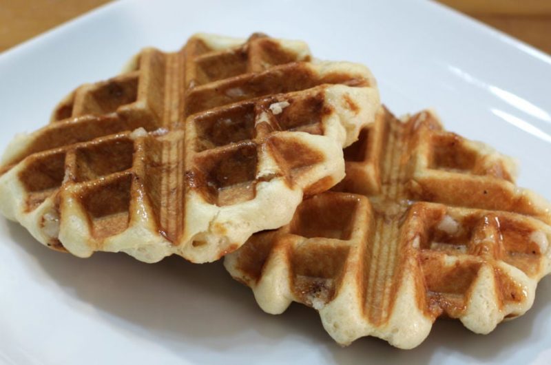 Two belgian sugar waffles on a white plate on a wooden table