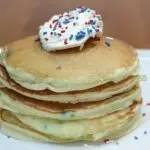 funfetti cake mix pancakes stacked on a white plate on a wooden table