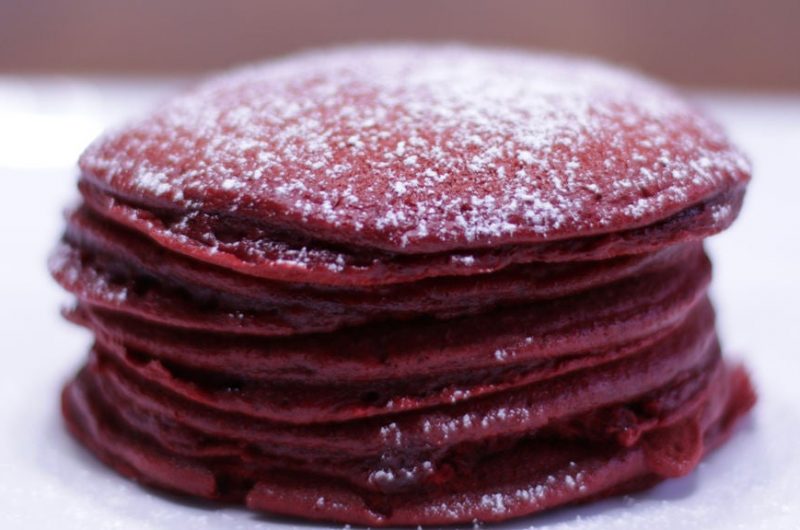 red velvet cake mix pancakes stacked on a white plate with powdered sugar on top
