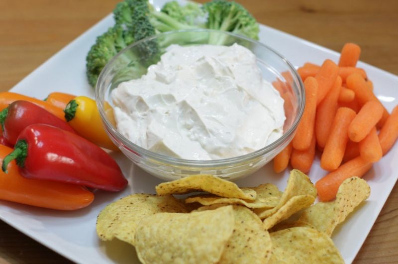Creamy garlic dip on a white square plate with veggies and chips