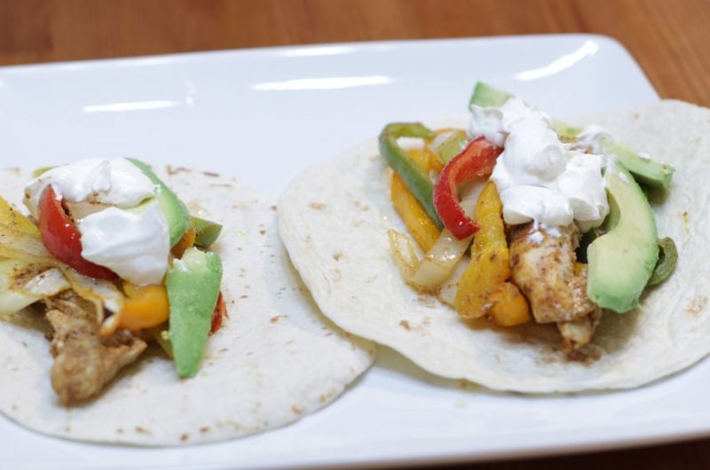 Sheet pan chicken fajitas on a white pate on a wooden table.