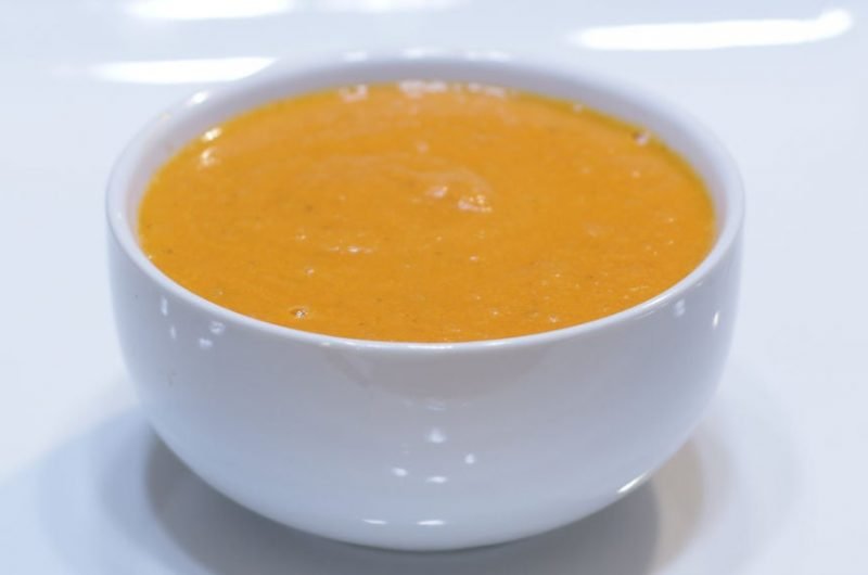 White bowl full of tomato soup on a white plate