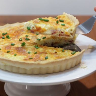 Bacon and cheese quiche in a tart pan on a white cake pedestal