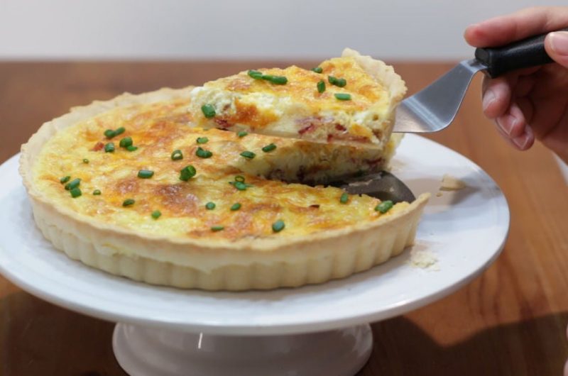 Bacon and cheese quiche in a tart pan on a white cake pedestal