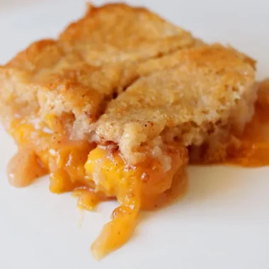 Slice of homemade peach cobbler on a white plate.