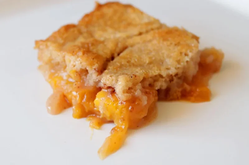 Slice of homemade peach cobbler on a white plate.