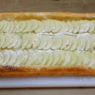 Apple tart puff pastry on a white cutting board on a wooden table