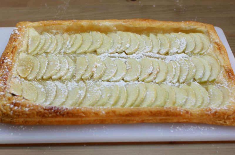 Apple tart puff pastry on a white cutting board on a wooden table
