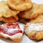 fry bread stacked on a white plate with strawberry jam and powdered sugar