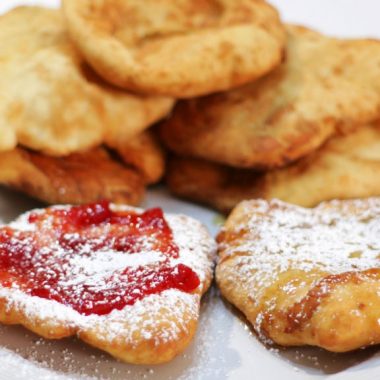 fry bread stacked on a white plate with strawberry jam and powdered sugar