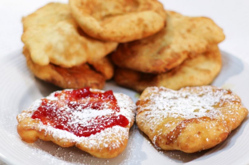 fry bread stacked on a white plate with strawberry jam and powdered sugar