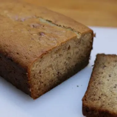 moist banana bread sliced on a white cutting board on a wooden table