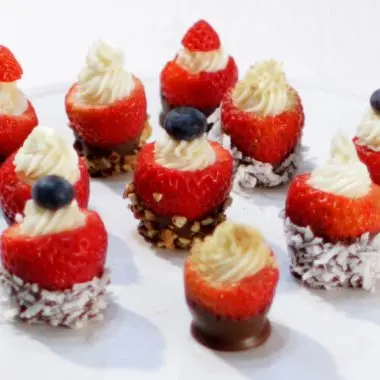 cheesecake stuffed chocolate dipped strawberries on a white cake pedestal.