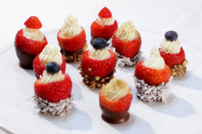 cheesecake stuffed chocolate dipped strawberries on a white cake pedestal.