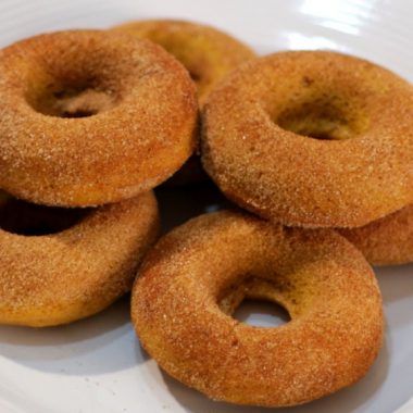 Pile of homemade pumpkin donuts on a white plate.