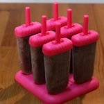 homemade fudgesicles in popsicle molds on a wooden table.