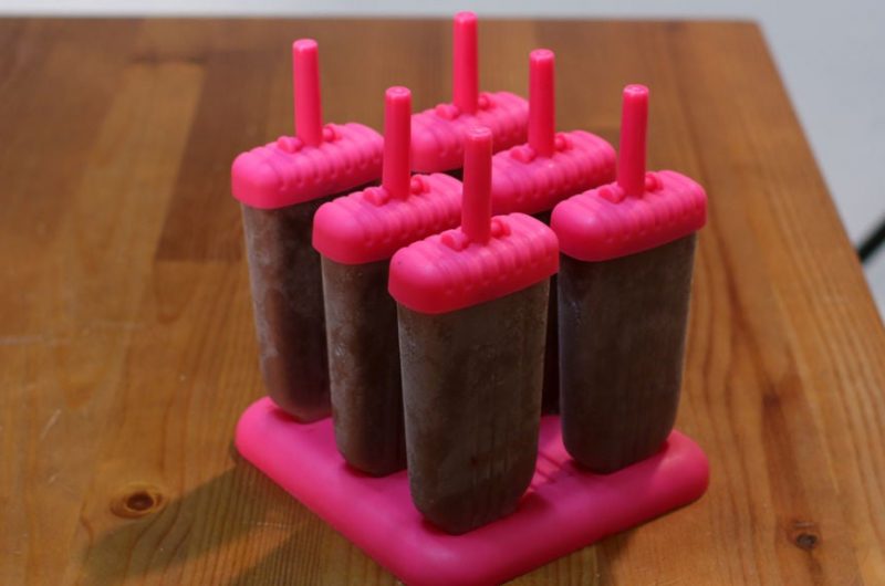 homemade fudgesicles in popsicle molds on a wooden table.