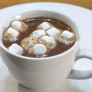 Homemade hot chocolate in a white mug on a white cake pedestal with marshmallows