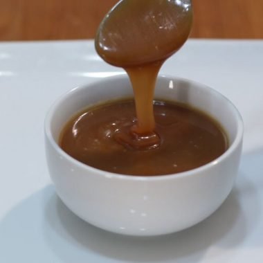 Homemade caramel sauce dripping off a spoon into a white bowl.
