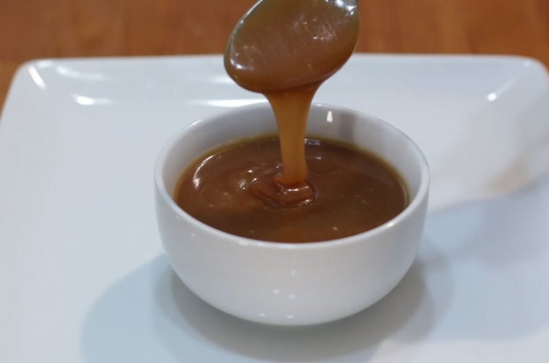 Homemade caramel sauce dripping off a spoon into a white bowl.