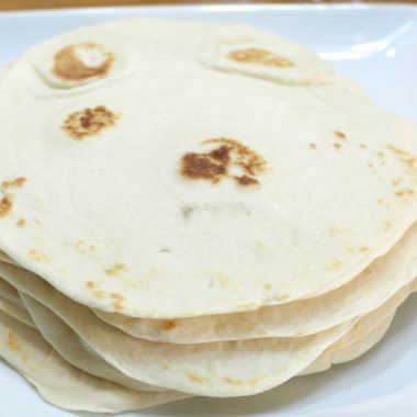 Homemade soft flour tortillas stacked on a white plate