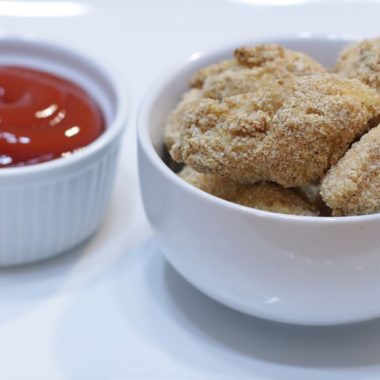Chicken nuggets in a white bowl next to ketchup