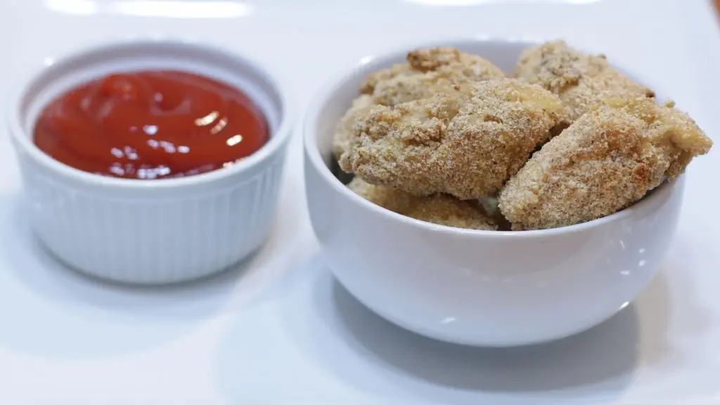 Chicken nuggets in a white bowl next to ketchup