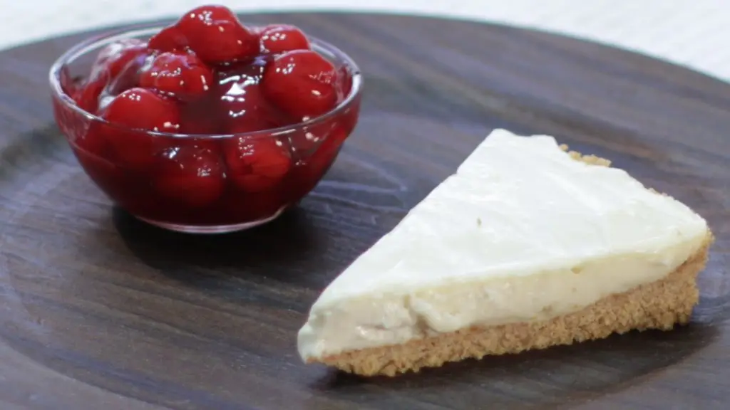 Slice of no-bake cheesecake on a plate next to bowl of cherries