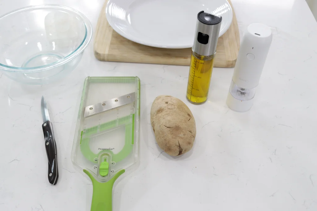 Potato next to a mandolin slicer on a white countertop Potato next to a mandolin slicer on a white countertop