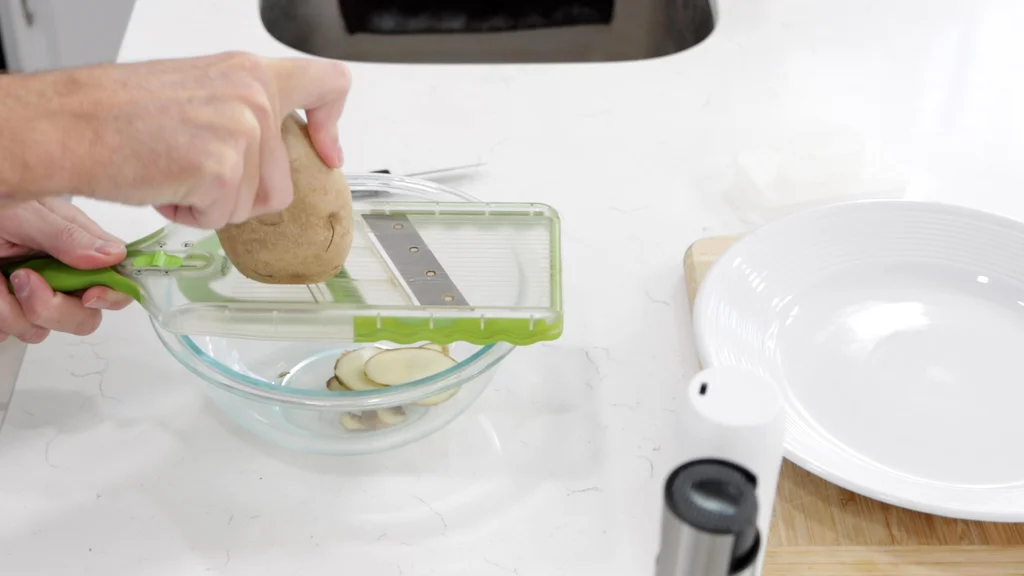 Hand slicing a washed potato with a mandolin slicer. Hand slicing potatoes on a mandolin