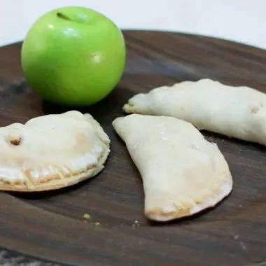 Three apple hand pies and a green apple on a brown plate.