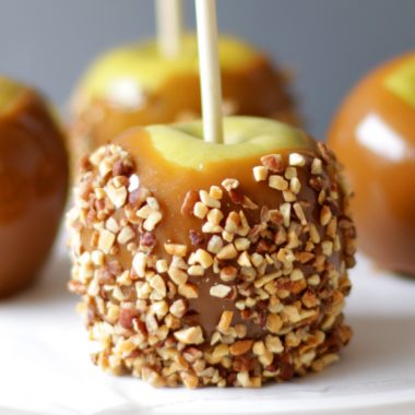 Four homemade caramel apples on a white plate