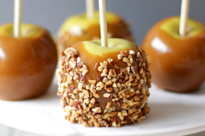 Four homemade caramel apples on a white plate